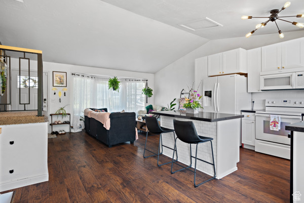 Kitchen with white appliances, lofted ceiling, dark wood-style flooring, white cabinets, and a breakfast bar