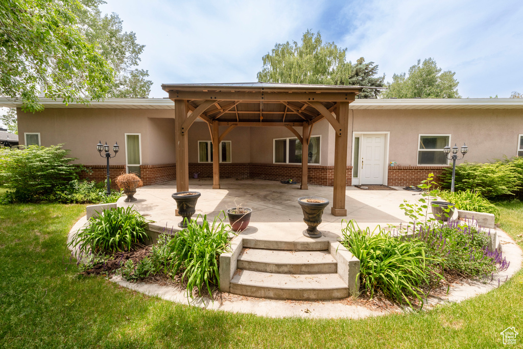 Back of house featuring stucco siding, brick siding, a patio area, and a lawn