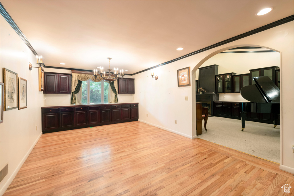 Unfurnished dining area featuring ornamental molding, light wood-type flooring, arched walkways, a chandelier, and baseboards