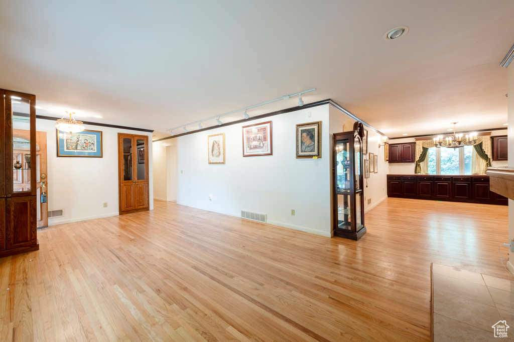 Unfurnished living room featuring a chandelier, light wood-type flooring, rail lighting, baseboards, and recessed lighting