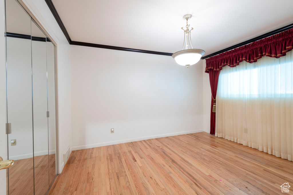 Unfurnished bedroom with wood finished floors, baseboards, crown molding, and a closet