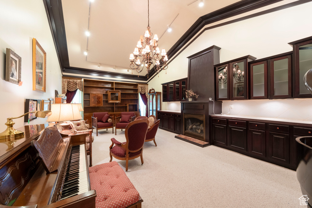 Living room featuring light carpet, a fireplace with raised hearth, crown molding, a chandelier, and track lighting