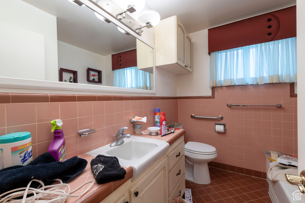Bathroom featuring vanity, plenty of natural light, tile patterned floors, tile walls, and toilet