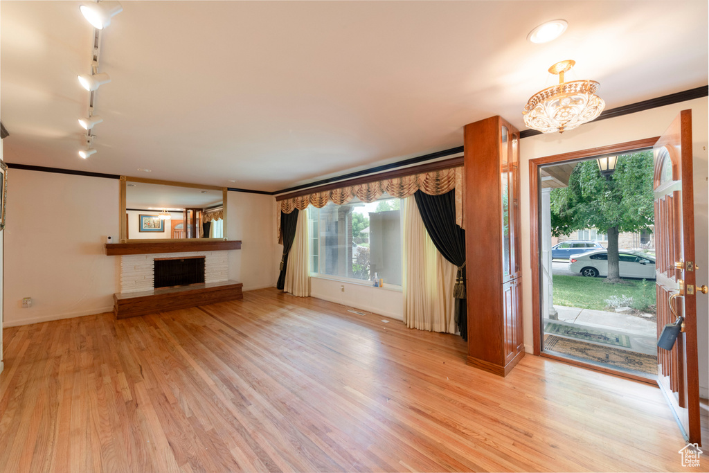 Unfurnished living room with a fireplace, wood finished floors, rail lighting, crown molding, and a chandelier