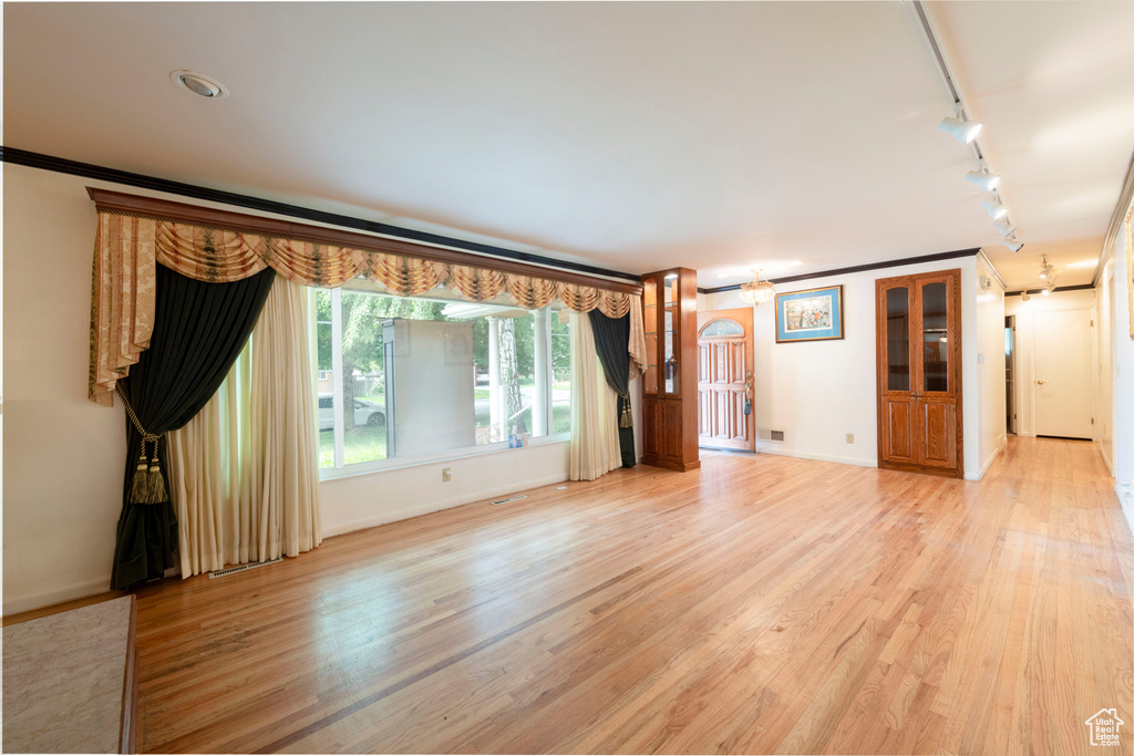 Unfurnished living room featuring rail lighting, baseboards, ornamental molding, and light wood finished floors