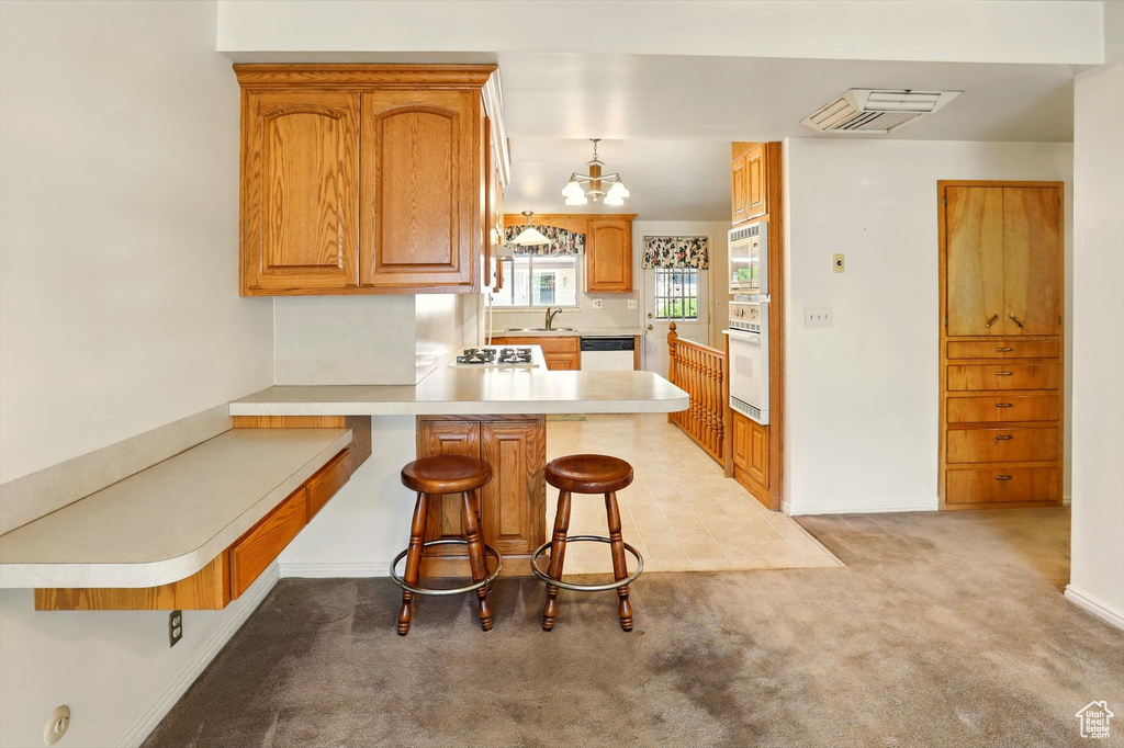Kitchen featuring appliances with stainless steel finishes, a sink, a peninsula, light colored carpet, and light countertops