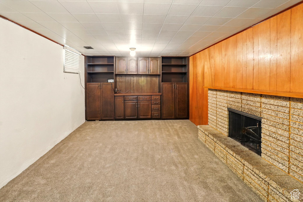 Unfurnished living room with light carpet, wood walls, and a fireplace