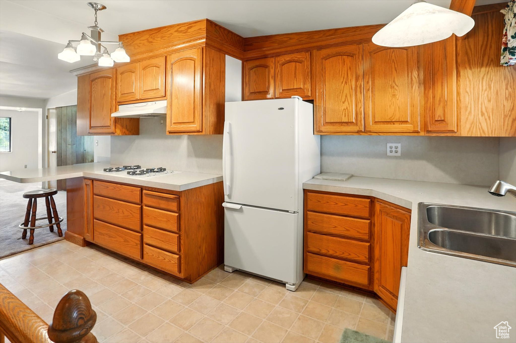 Kitchen featuring white appliances, a sink, light countertops, under cabinet range hood, and brown cabinets