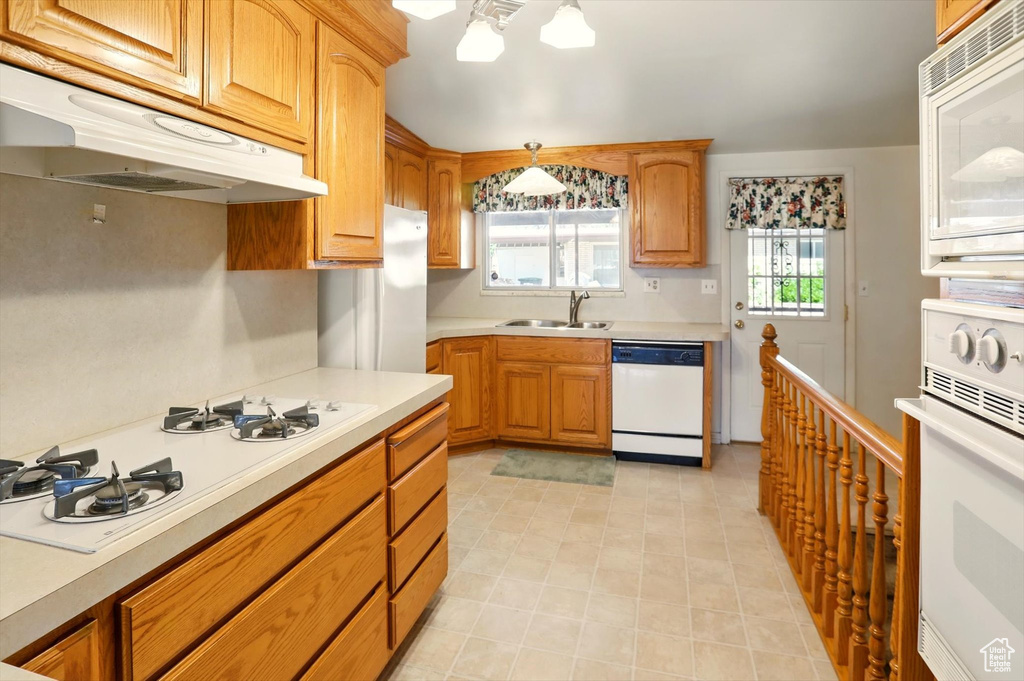 Kitchen with white appliances, under cabinet range hood, a sink, light countertops, and light tile patterned flooring