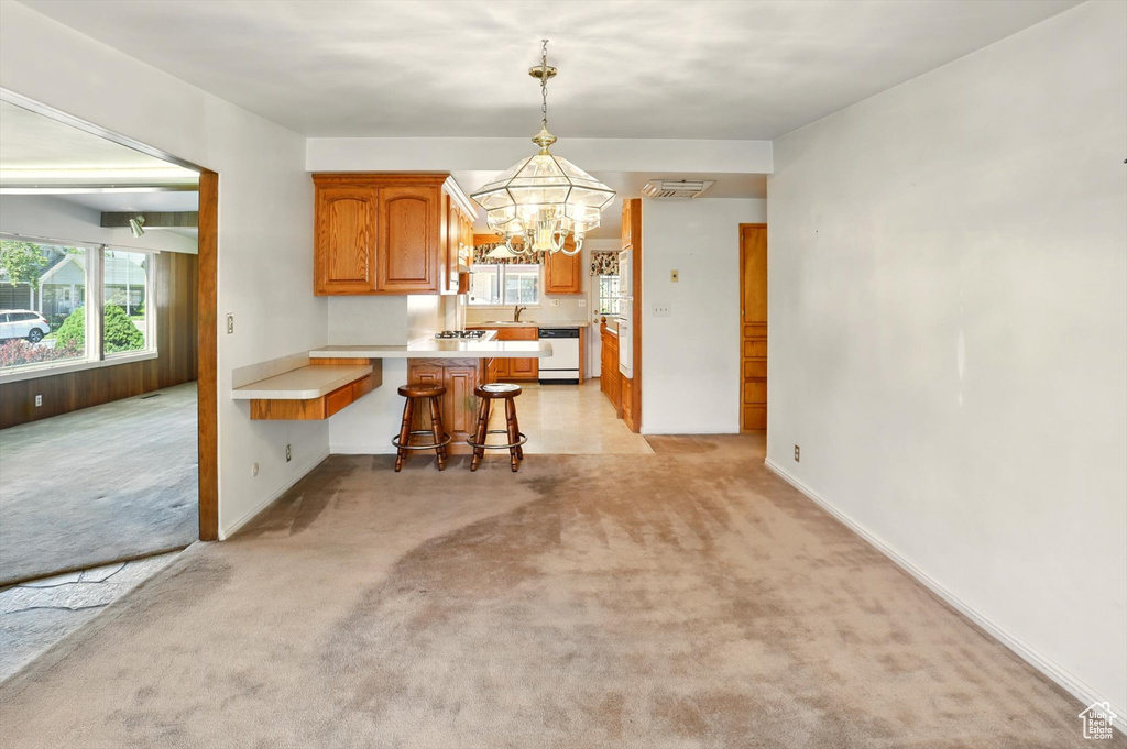 Kitchen with dishwasher, a chandelier, a peninsula, light carpet, and light countertops