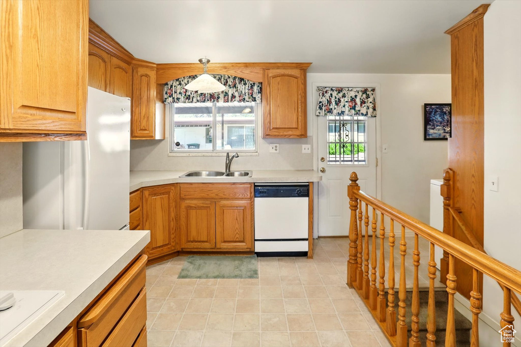 Kitchen featuring white appliances, a sink, light countertops, light tile patterned floors, and brown cabinetry