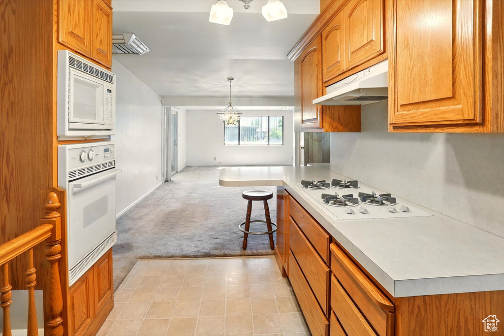 Kitchen with white appliances, under cabinet range hood, light carpet, a chandelier, and light countertops