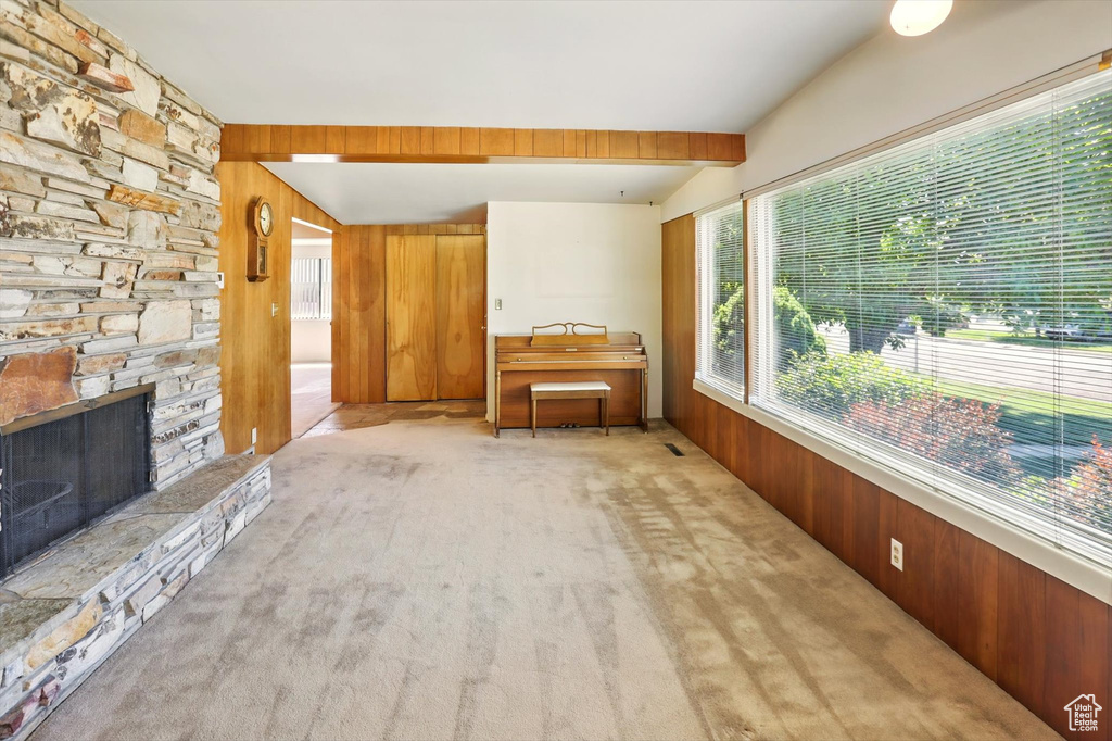 Carpeted living area with wooden walls, beamed ceiling, and a fireplace