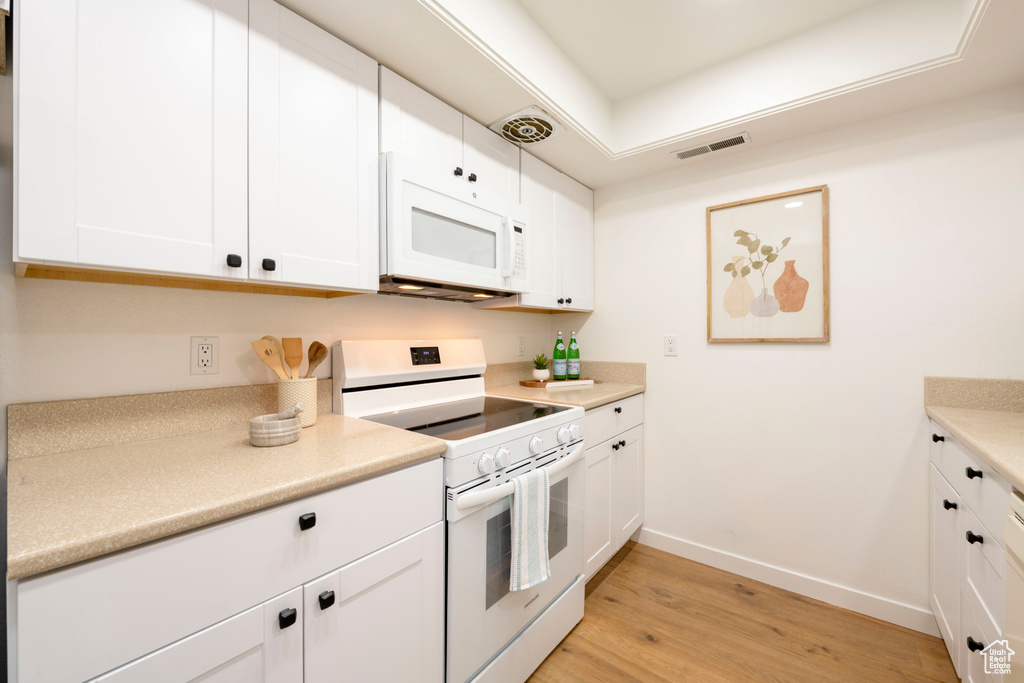 Kitchen with white appliances, baseboards, light wood-style floors, light countertops, and white cabinetry