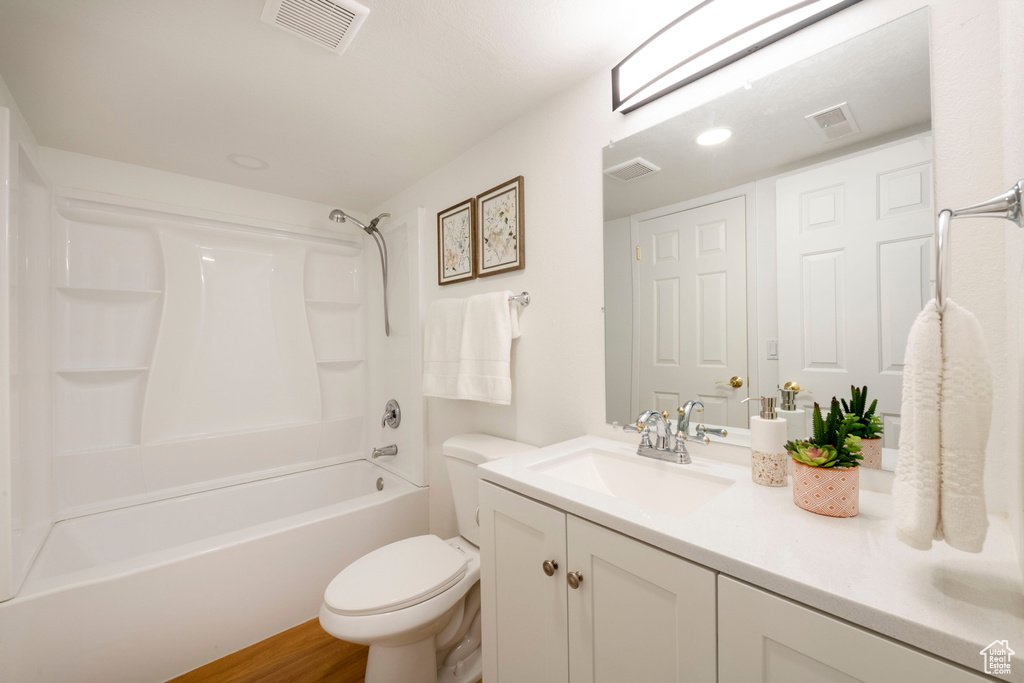 Bathroom featuring double vanity, toilet, shower / washtub combination, and wood finished floors