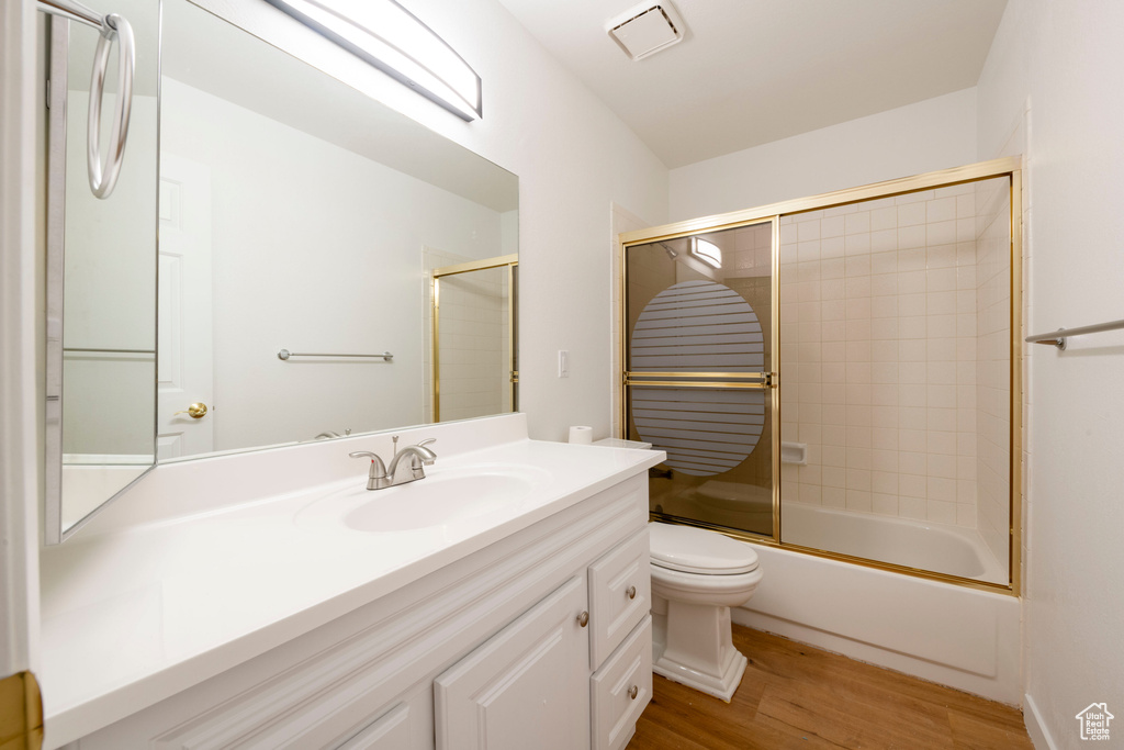 Bathroom featuring toilet, vanity, wood finished floors, and bath / shower combo with glass door