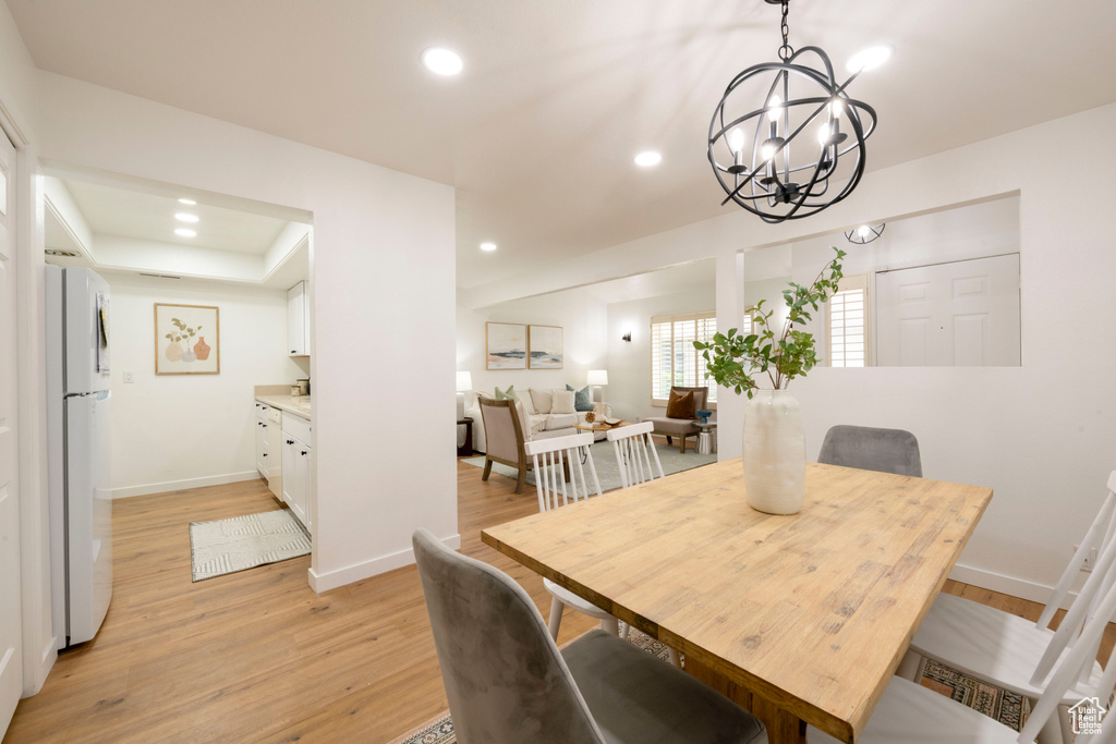 Dining space with light wood-style flooring, a chandelier, recessed lighting, baseboards, and a tray ceiling