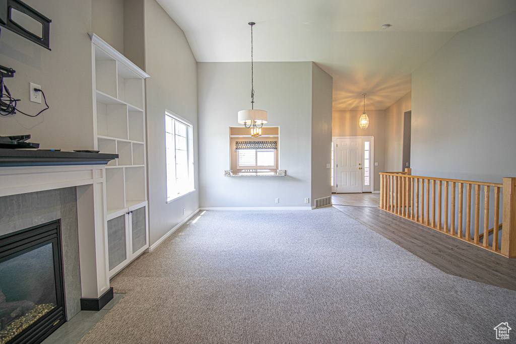 Unfurnished living room with carpet floors, a chandelier, a tiled fireplace, baseboards, and high vaulted ceiling