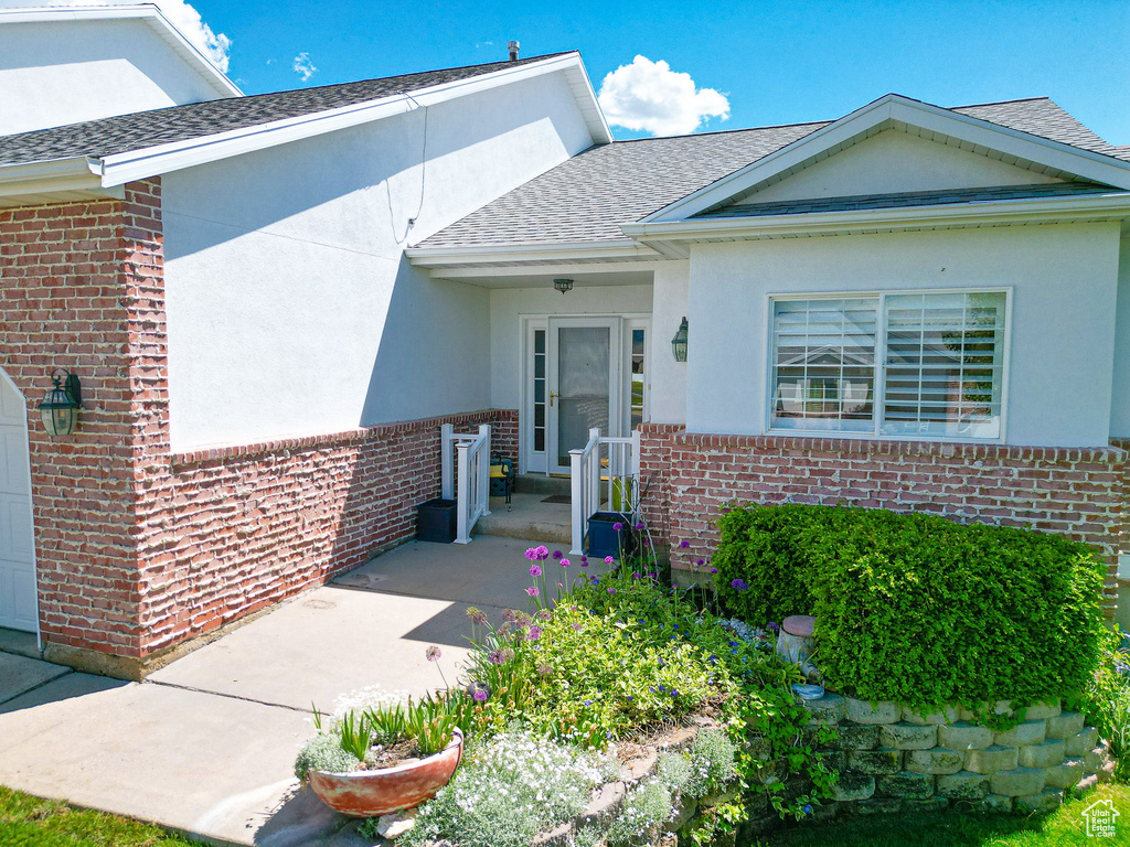 Doorway to property with brick siding, a shingled roof, and stucco siding