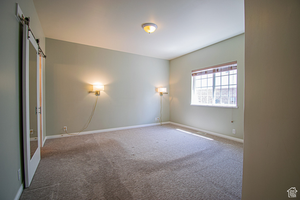 Carpeted empty room with a barn door and baseboards