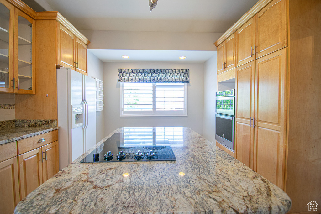 Kitchen with white fridge with ice dispenser, double oven, light stone counters, glass insert cabinets, and black electric stovetop