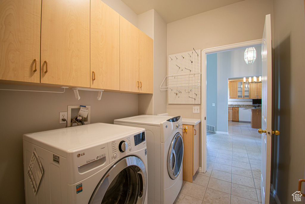 Laundry room featuring washer and dryer, cabinet space, light tile patterned floors, and baseboards