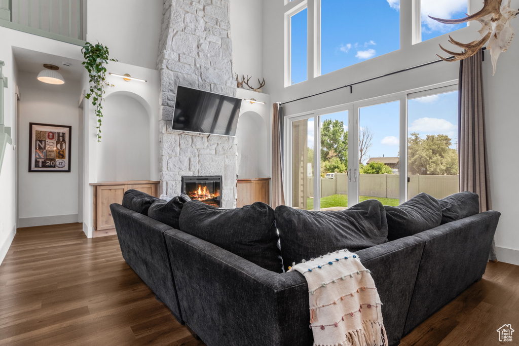 Living room with a stone fireplace, a high ceiling, dark wood-type flooring, and baseboards