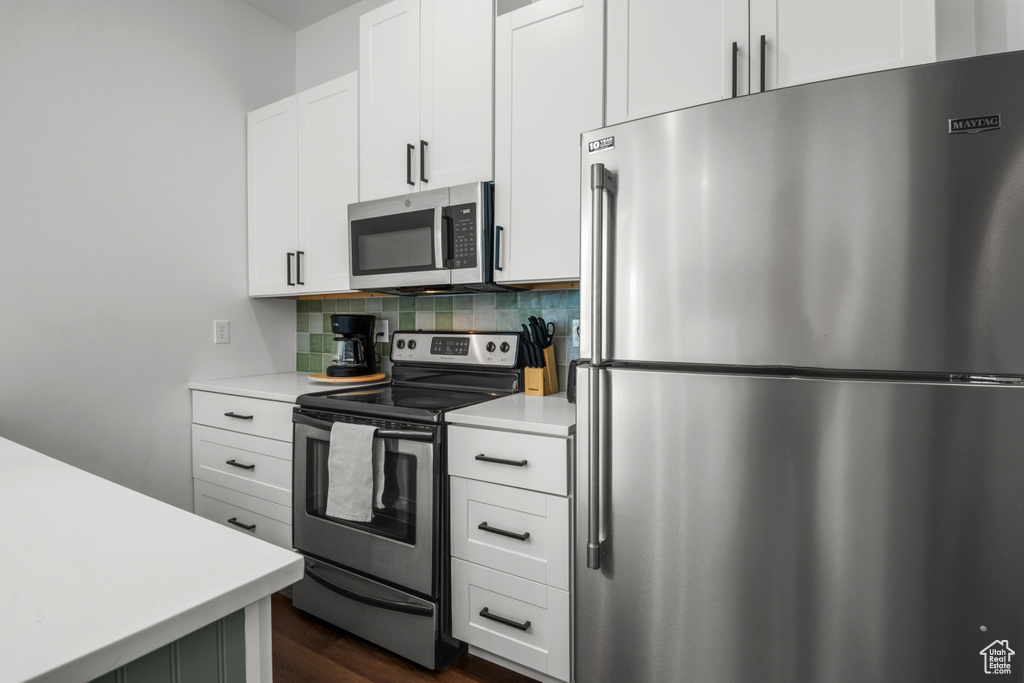 Kitchen featuring stainless steel appliances, light countertops, dark wood-style flooring, backsplash, and white cabinetry