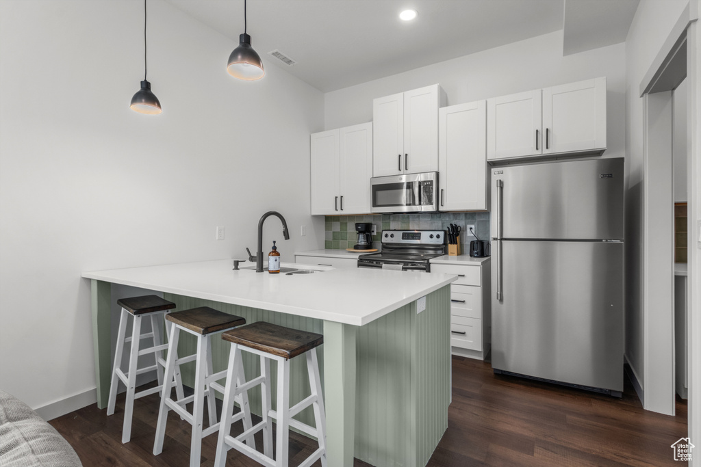 Kitchen featuring stainless steel appliances, a sink, tasteful backsplash, a breakfast bar, and dark wood-style floors