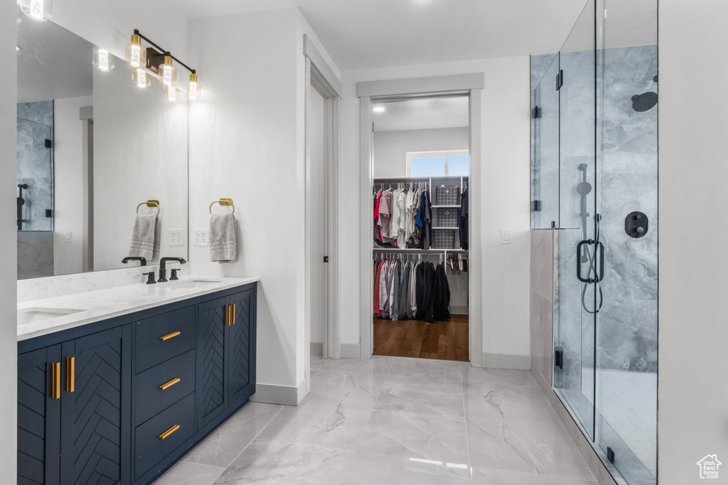 Bathroom featuring double vanity, a stall shower, marble finish floors, baseboards, and a walk in closet