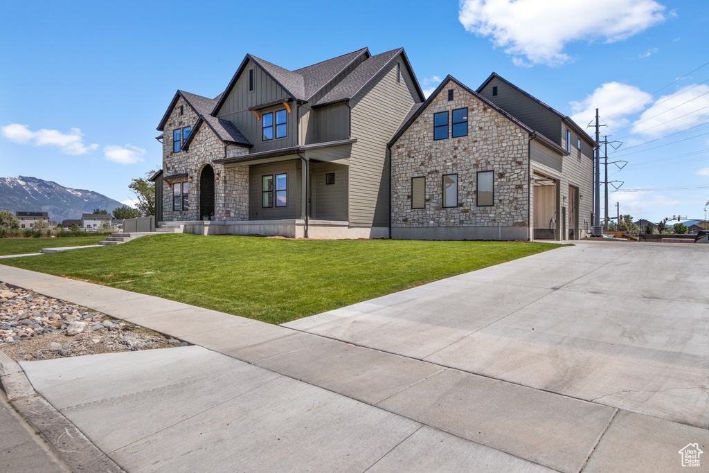 Craftsman house with stone siding, board and batten siding, a front yard, and driveway