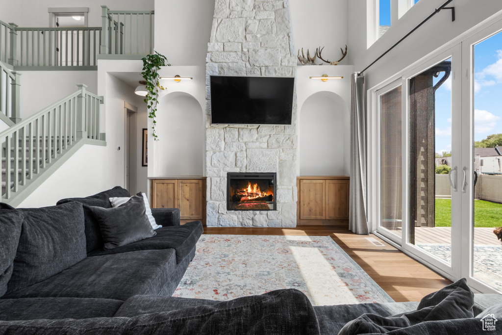 Living area with wood finished floors, a stone fireplace, a high ceiling, and stairs