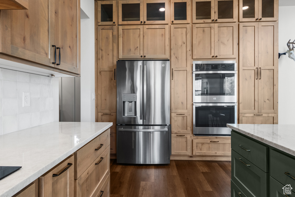 Kitchen featuring appliances with stainless steel finishes, dark wood-style flooring, tasteful backsplash, light stone countertops, and glass insert cabinets