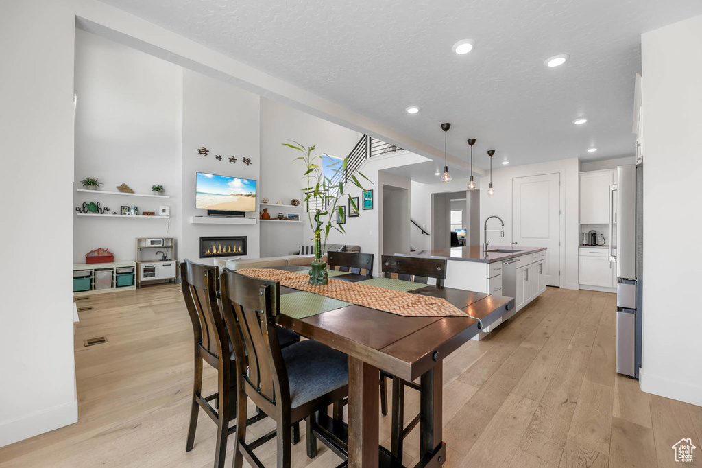 Dining room featuring light wood-type flooring, a glass covered fireplace, recessed lighting, baseboards, and a textured ceiling