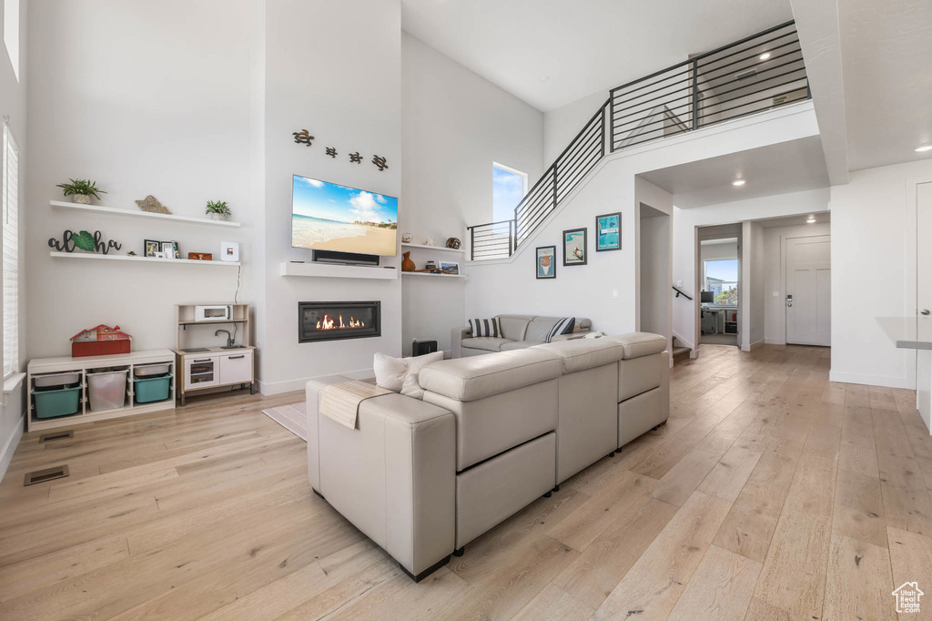 Living area featuring a high ceiling, a glass covered fireplace, light wood-style floors, and baseboards