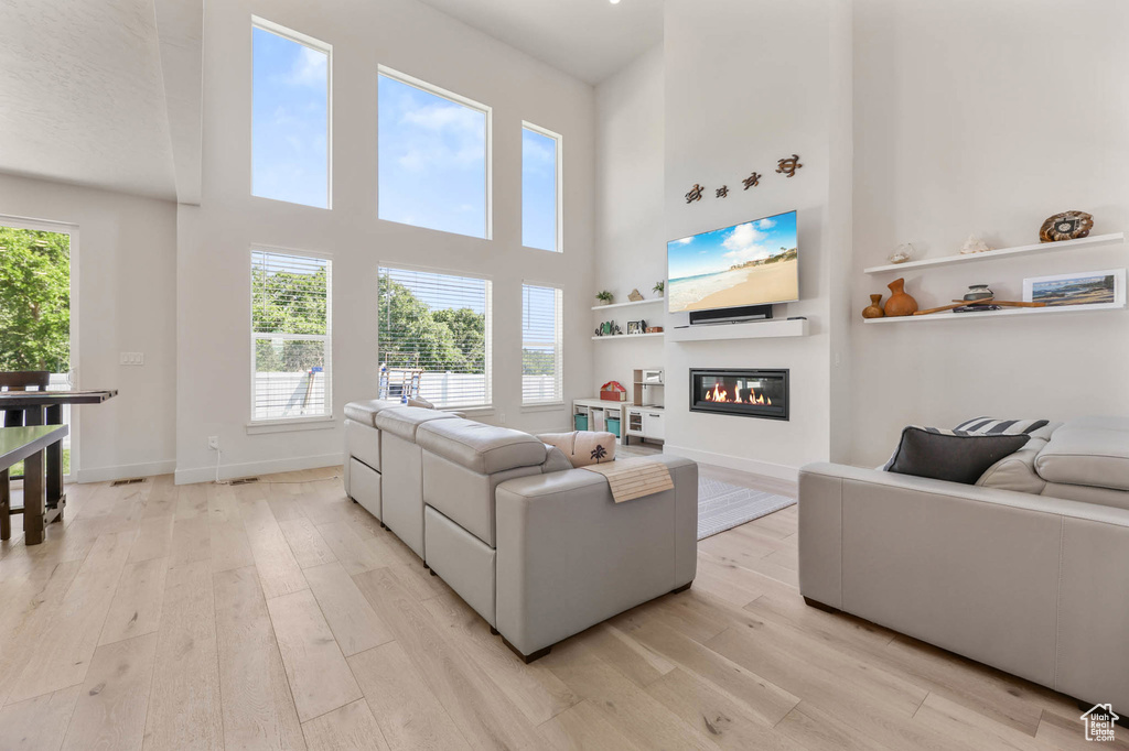Living area featuring light wood finished floors, a glass covered fireplace, a towering ceiling, and baseboards