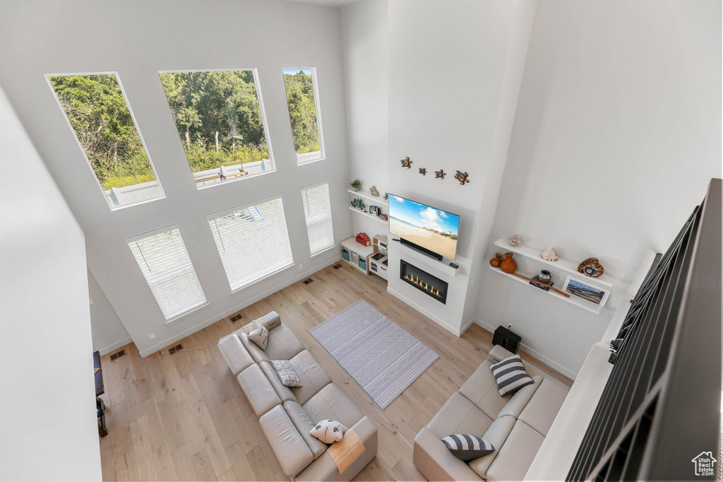 Living room with a towering ceiling, healthy amount of natural light, a glass covered fireplace, and wood finished floors