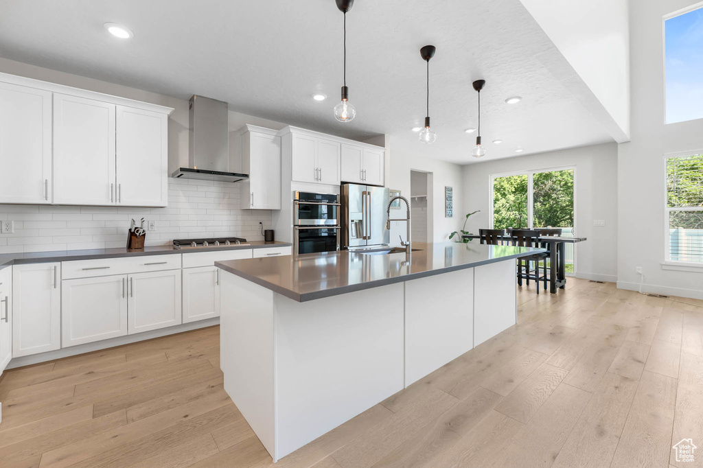 Kitchen featuring wall chimney range hood, appliances with stainless steel finishes, light wood-type flooring, dark countertops, and recessed lighting