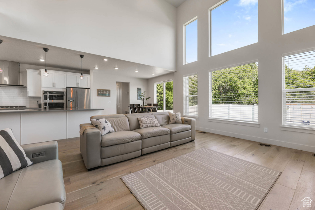 Living room with healthy amount of natural light, light wood-style floors, a high ceiling, baseboards, and recessed lighting