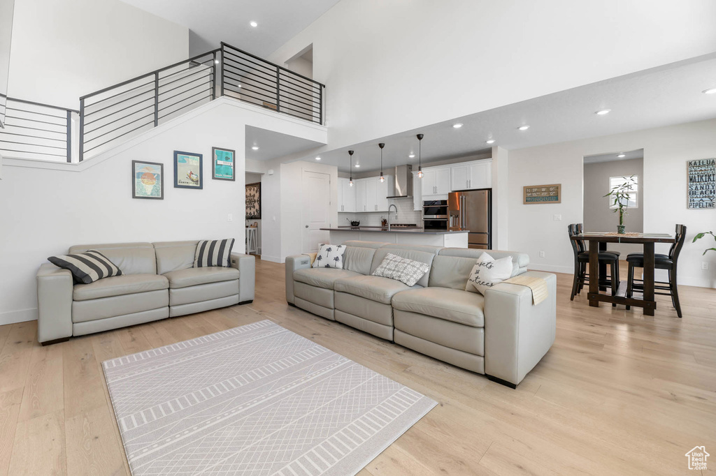 Living room with light wood finished floors, a high ceiling, baseboards, recessed lighting, and stairs