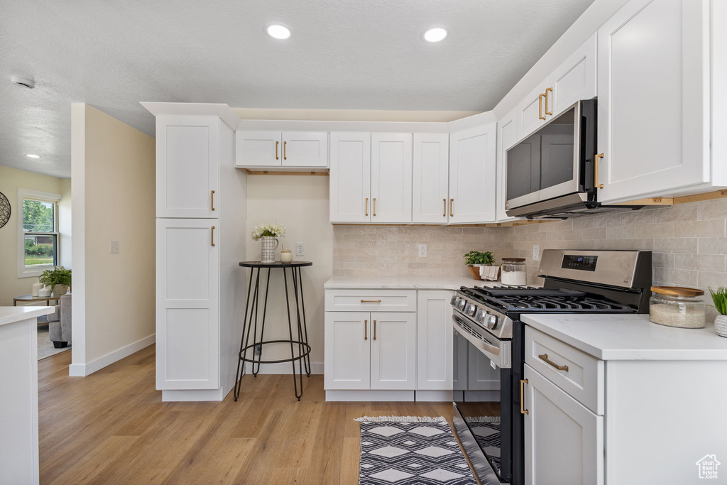 Kitchen featuring appliances with stainless steel finishes, light wood-style floors, white cabinetry, light countertops, and decorative backsplash