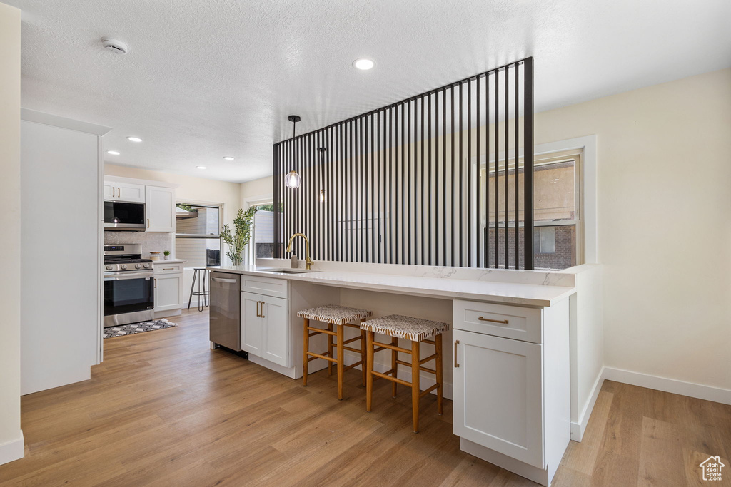 Kitchen with appliances with stainless steel finishes, light wood finished floors, white cabinetry, a kitchen breakfast bar, and light countertops