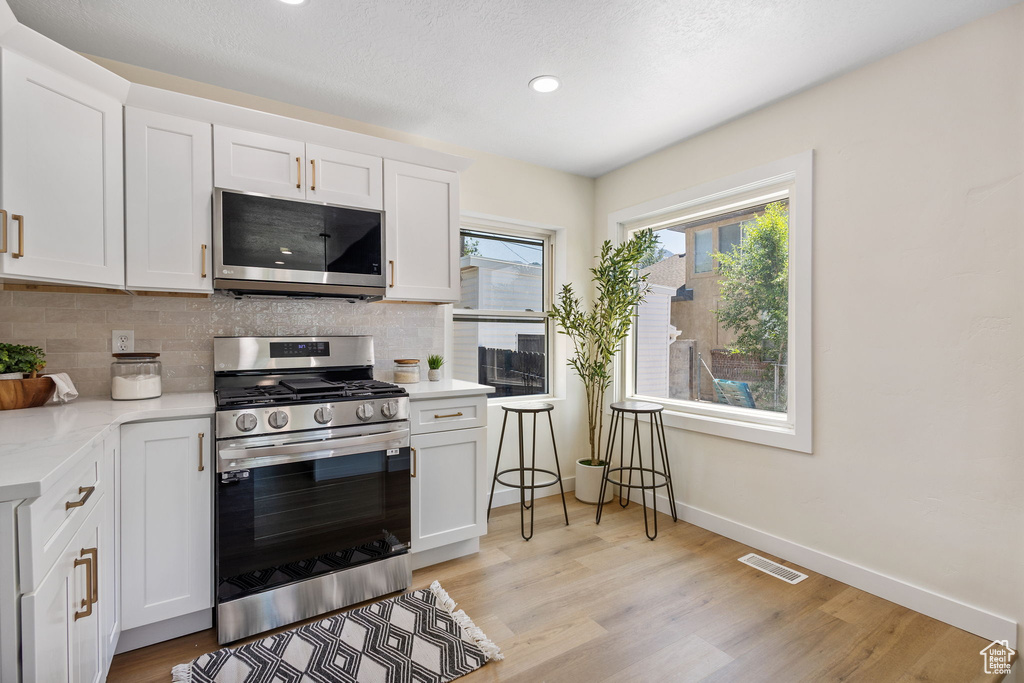 Kitchen featuring appliances with stainless steel finishes, tasteful backsplash, light countertops, white cabinetry, and light wood-style flooring