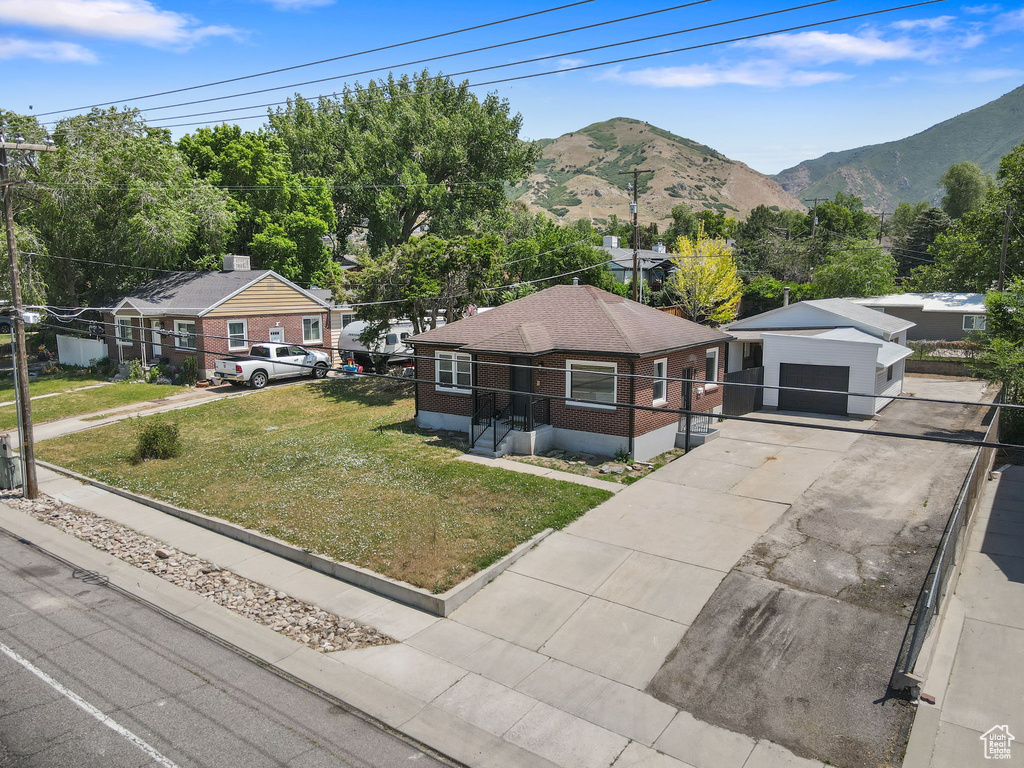View of front facade with a detached garage, a front yard, a mountain view, and driveway
