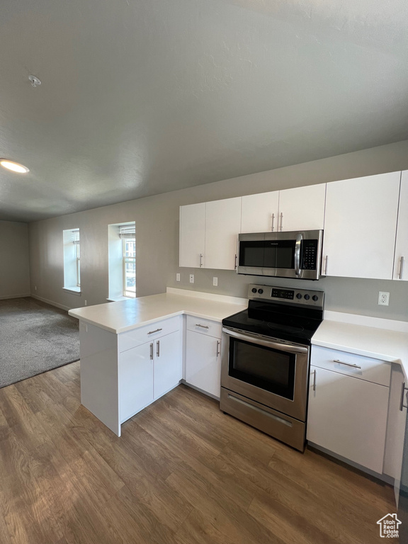 Kitchen featuring stainless steel appliances, dark wood-style flooring, open floor plan, white cabinets, and light countertops