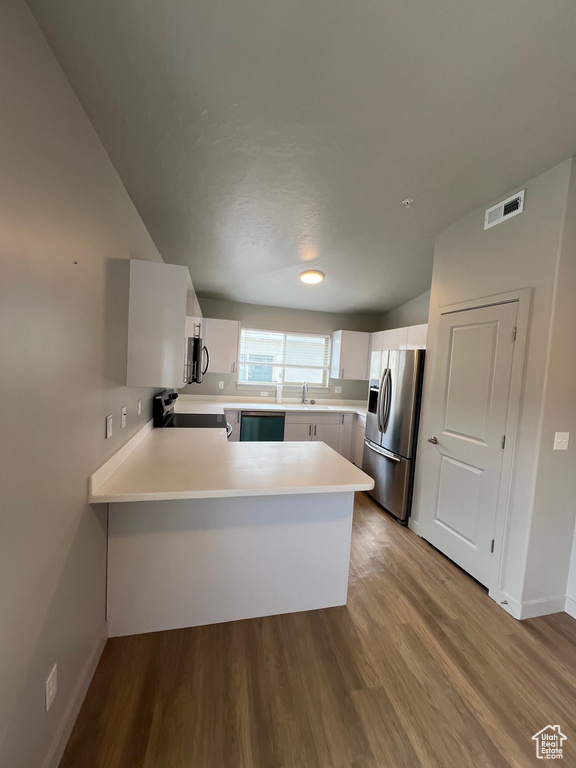 Kitchen with appliances with stainless steel finishes, a sink, light countertops, a peninsula, and baseboards