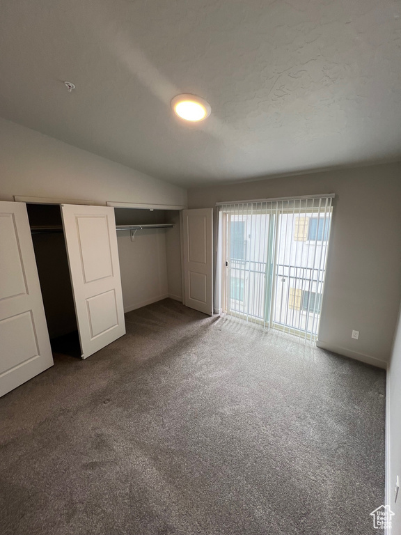 Unfurnished bedroom featuring carpet flooring, two closets, vaulted ceiling, baseboards, and access to exterior