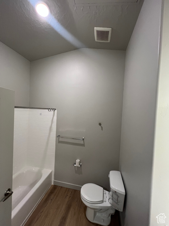 Bathroom with wood finished floors, toilet, baseboards, a bath, and lofted ceiling
