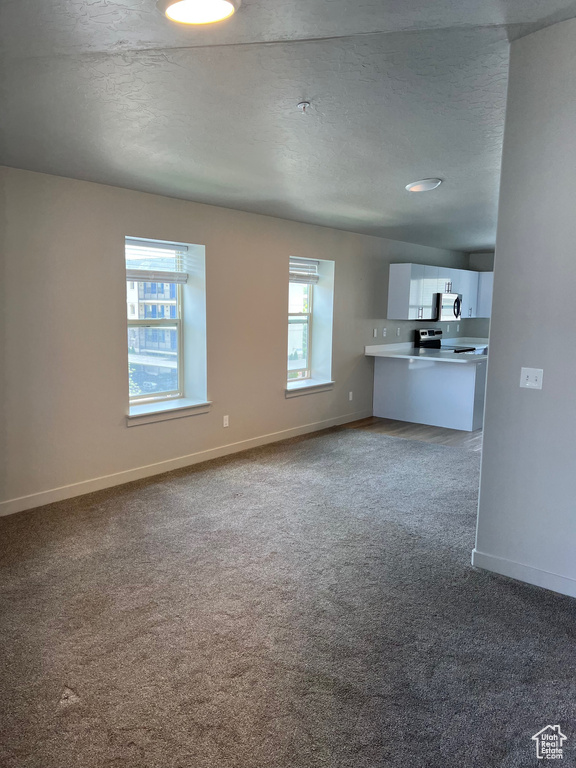 Unfurnished living room featuring carpet, baseboards, and a textured ceiling