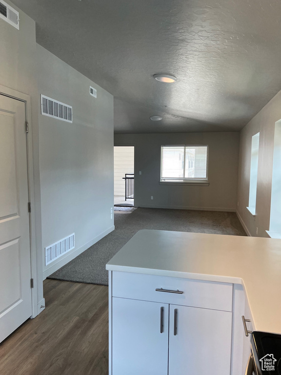 Kitchen with light countertops, white cabinets, baseboards, dark wood finished floors, and a textured ceiling